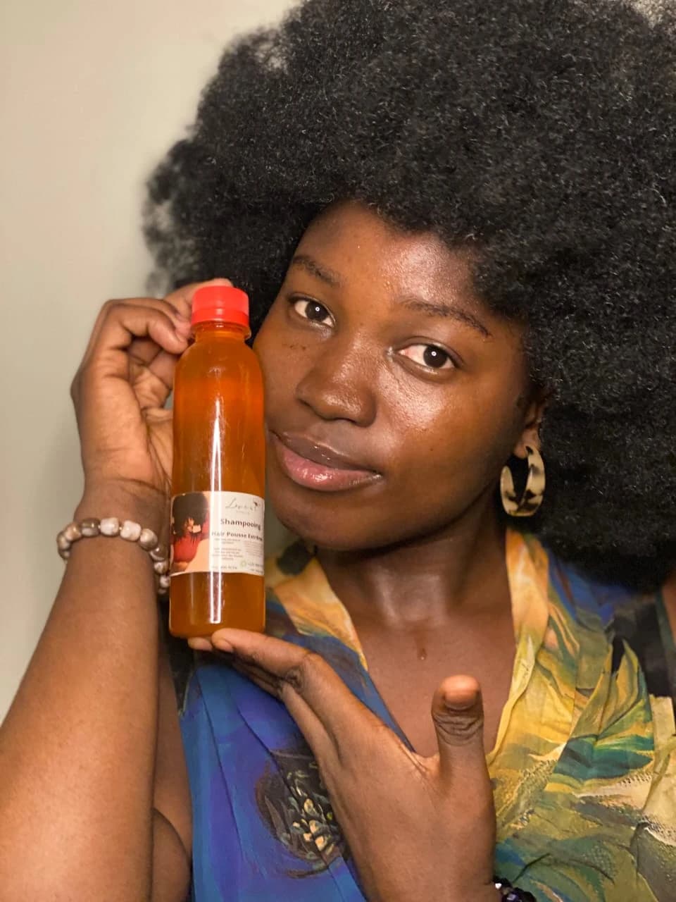 Femme aux cheveux afro naturels tenant un flacon de shampooing contre sa joue