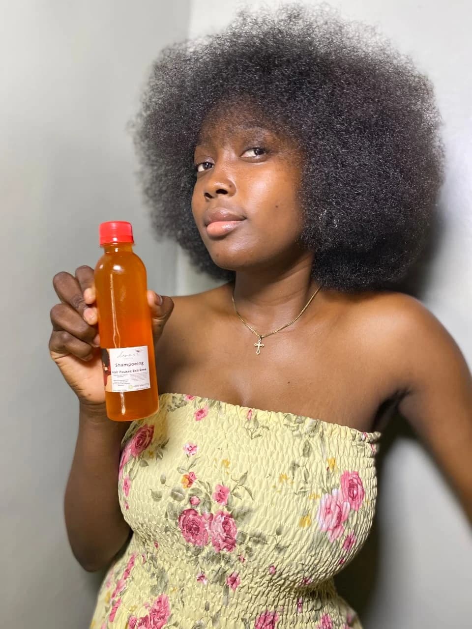 Femme à l'afro volumineux présentant un flacon de shampooing